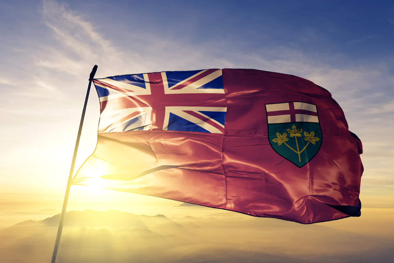 Ontario flag flies against a sunset sky, golden sun illuminating it from behind. PokerStars Ontario Online Poker, Casino, & Sports Betting Launch Gets Closer