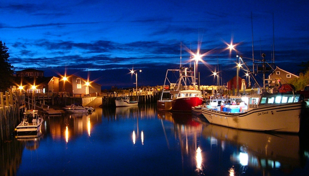 Nova Scotia harbor at night, with lit up boats at the dock, underneath a dark starlit sky. Nova Scotians recently got access to Single-Event Sports Betting.