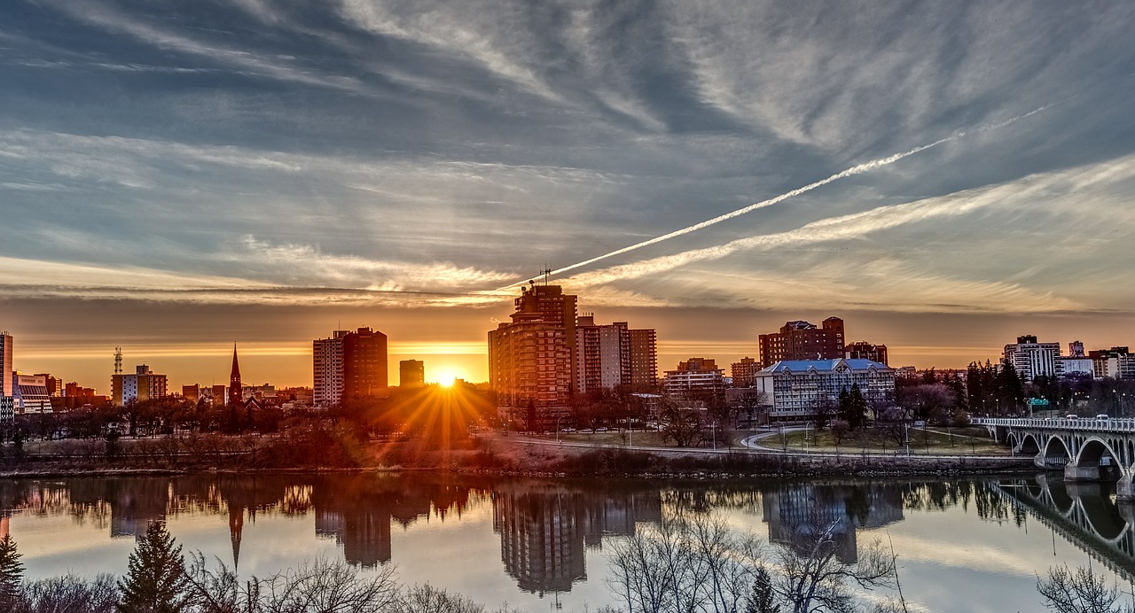 beautiful scenic view of Saskatoon, Saskatchewan at sunset with the sun shining behind the buildings of downtown and reflecting on the river.